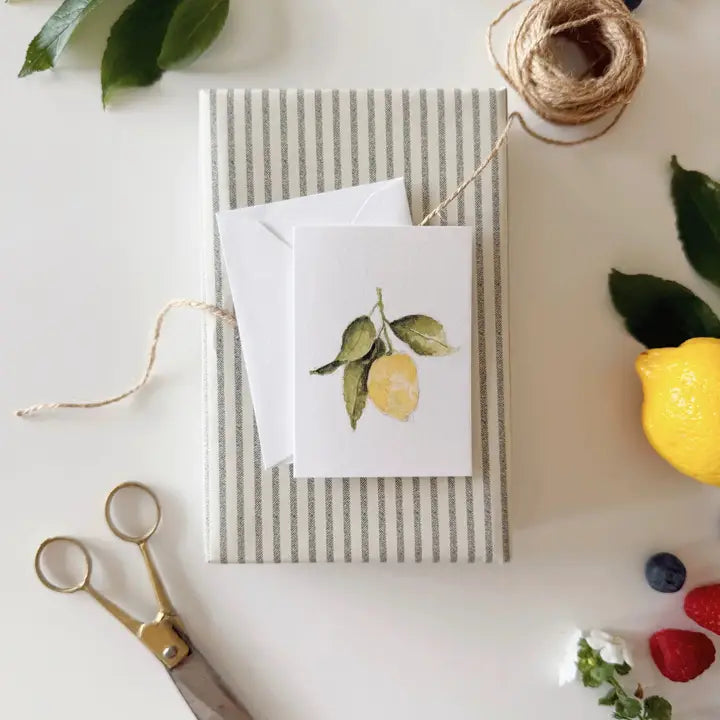 Greeting card with lemon design on a striped envelope, surrounded by decorative items on a white surface.