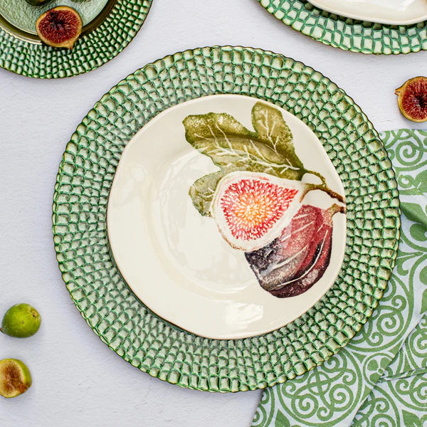Decorative plate with fig design on a matching green rim, surrounded by whole figs.