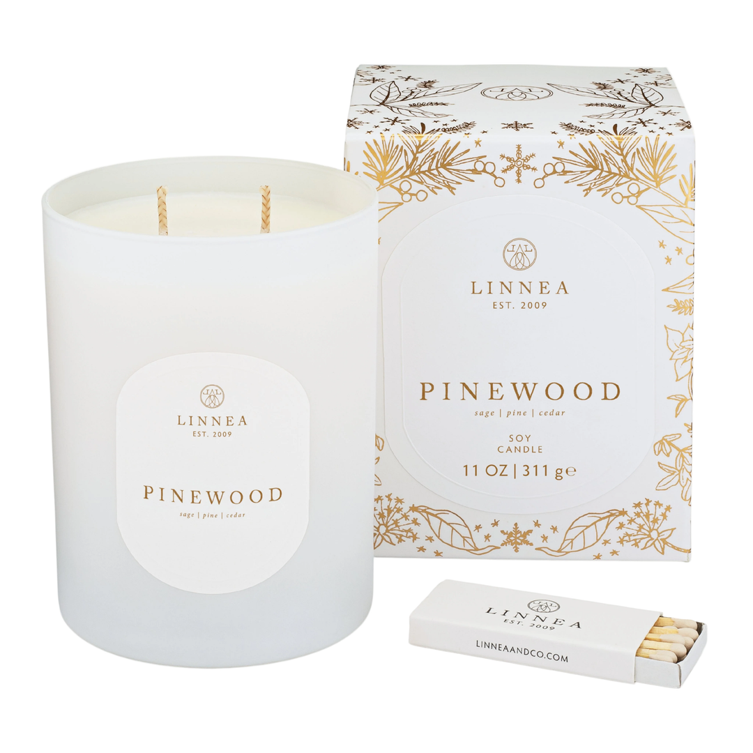 LINNEA Pinewood candle with gilded holiday packaging and matches on a white background