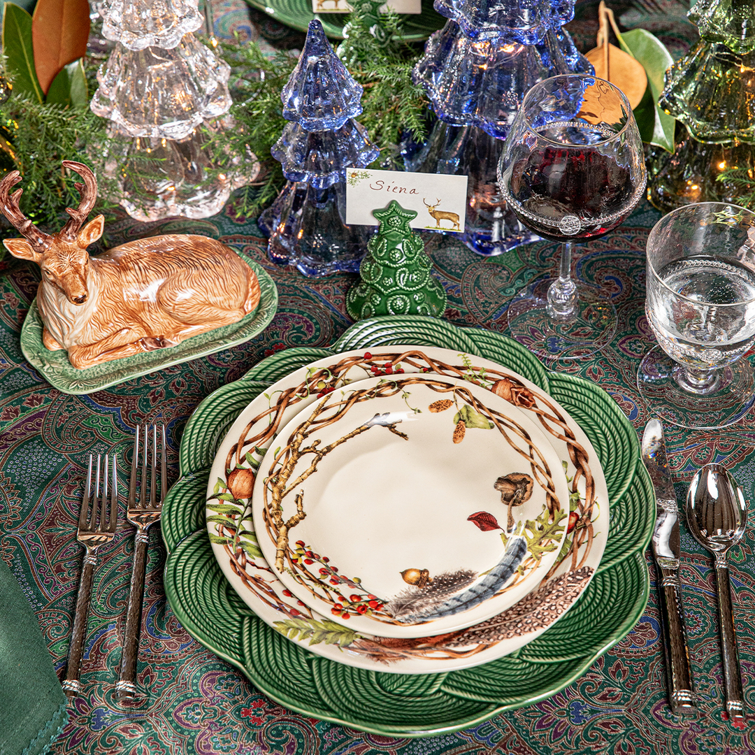 Decorative table setting with a nature-themed plate, deer figurine, and Christmas tree decorations.