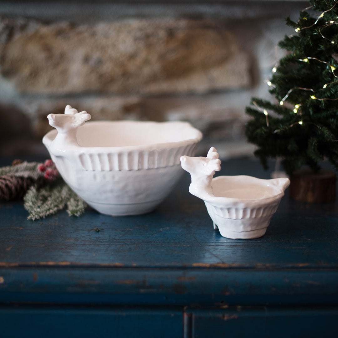 Two ceramic reindeer shaped bowls on a wooden surface with a festive background