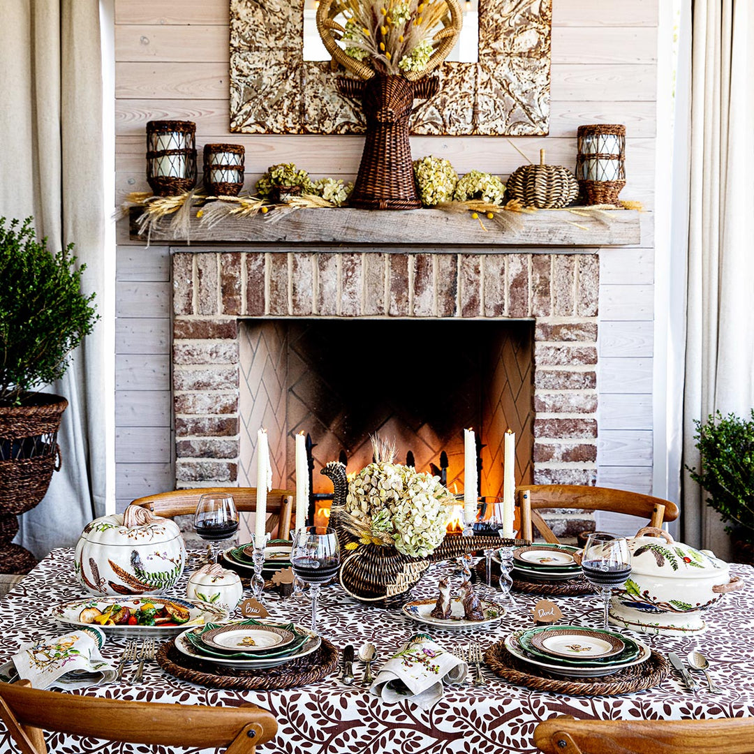 Juliska forest walk items on a table with a hydrangea floral arrangement in front of a fireplace with wicker candleholders and a wicker stag head vase
