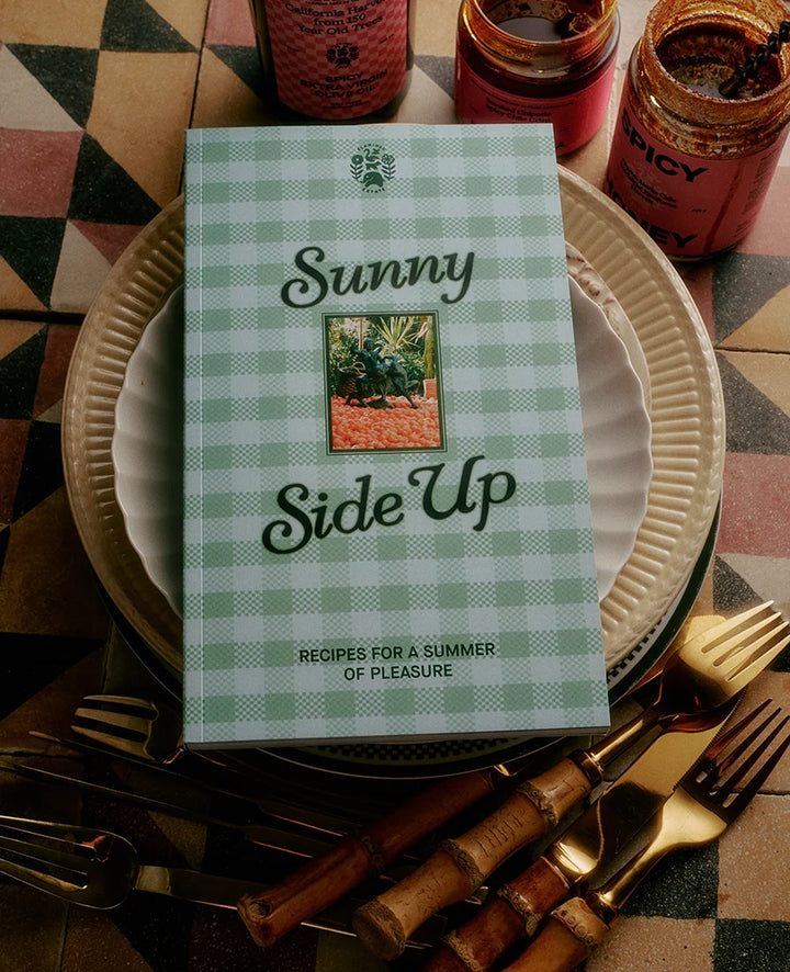 Cookbook titled 'Sunny Side Up' on a table with plates and utensils.