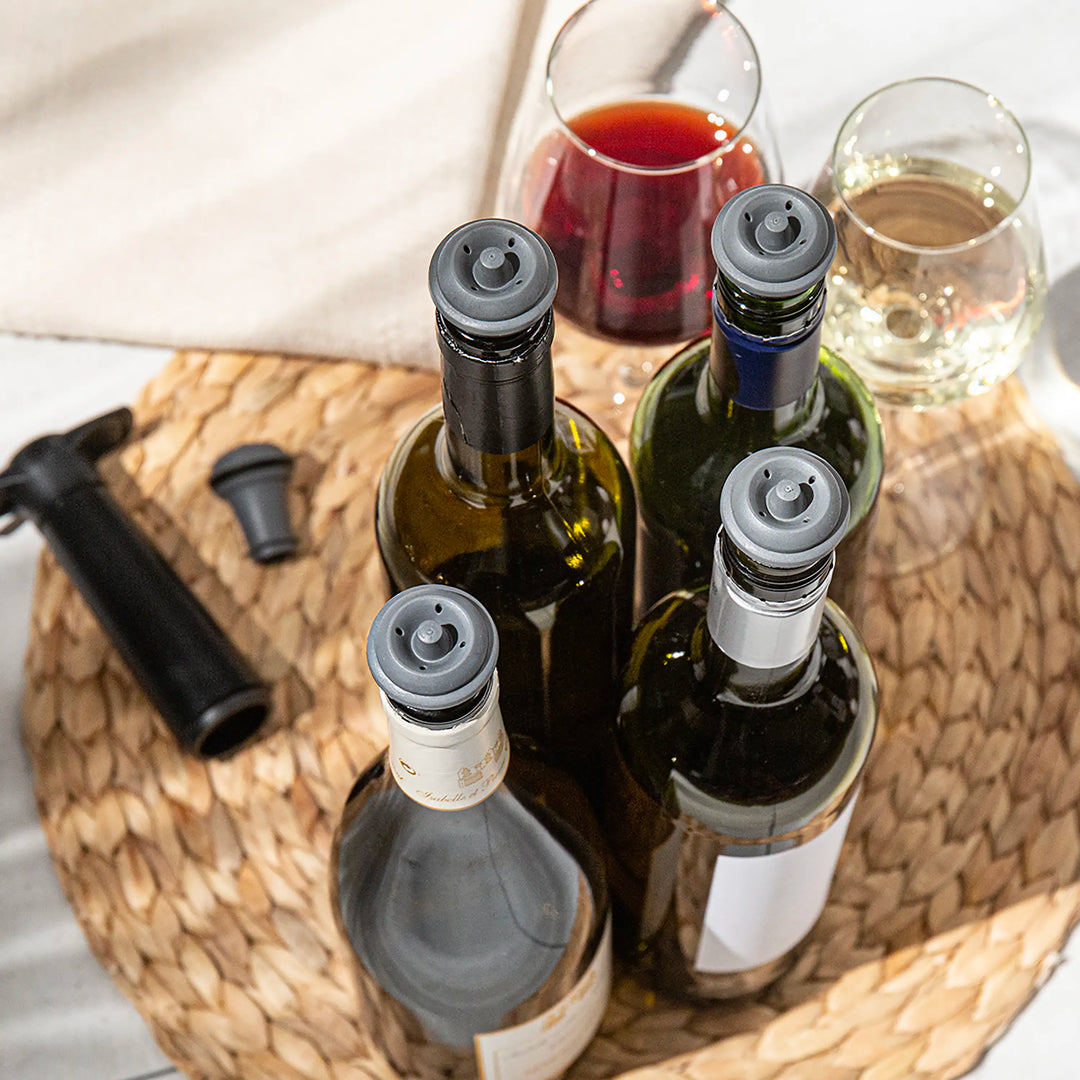 Wine bottles with grey vacuum seal stoppers and glasses on a woven tray with a white napkin.