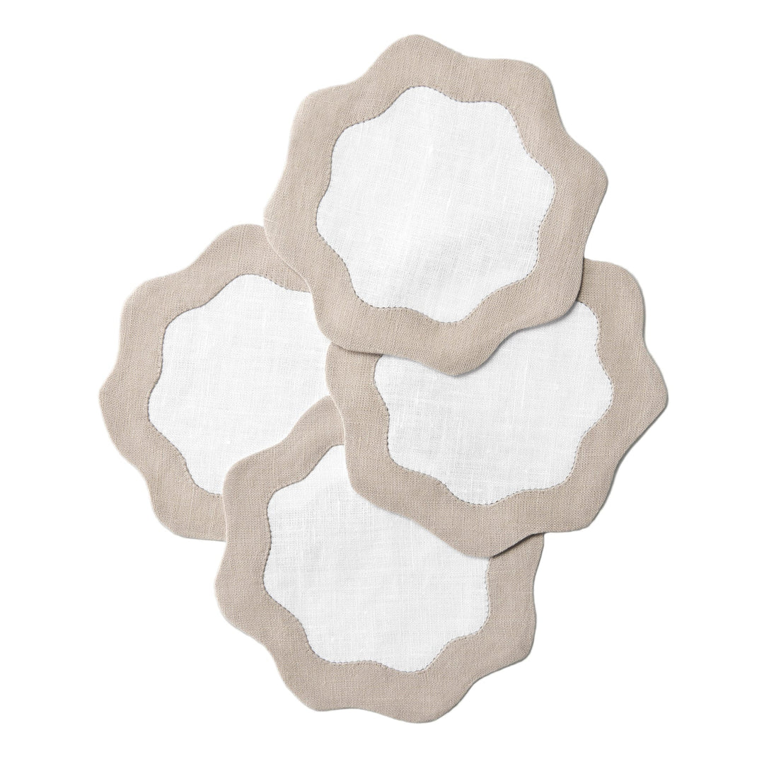 Four white coasters with sandy off white wavy edges on a white surface