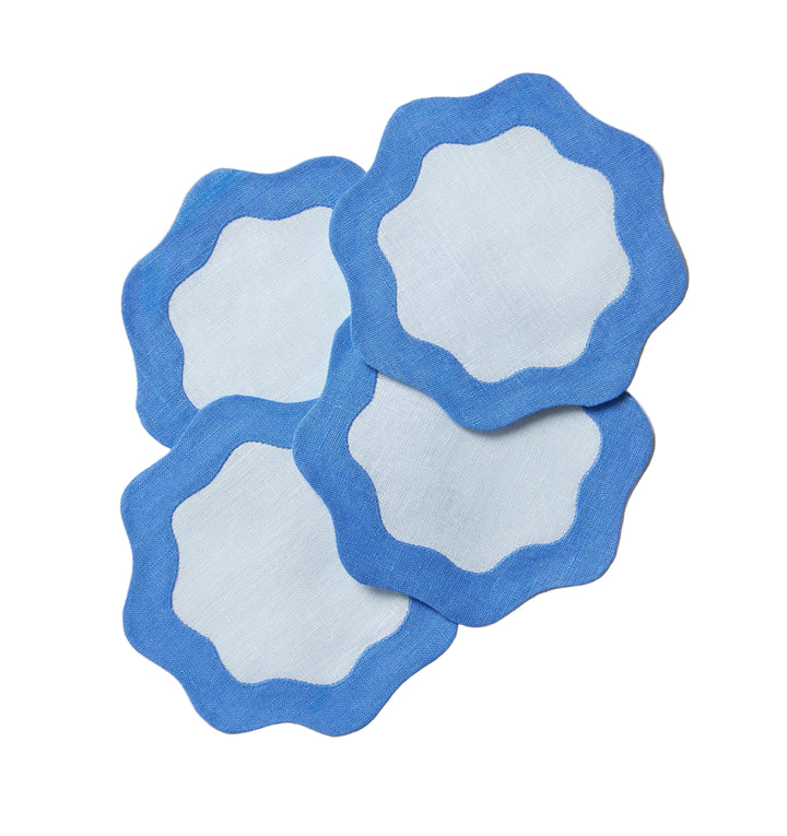 Four blue coasters with light blue centers and wavy edges on a light gray surface