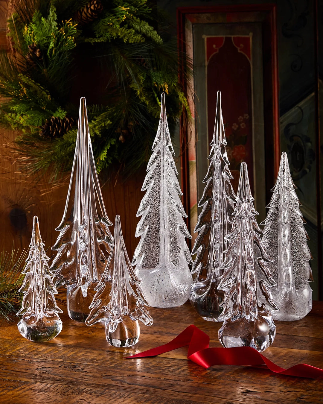 Set of clear glass Christmas trees on a wooden surface with a red ribbon.
