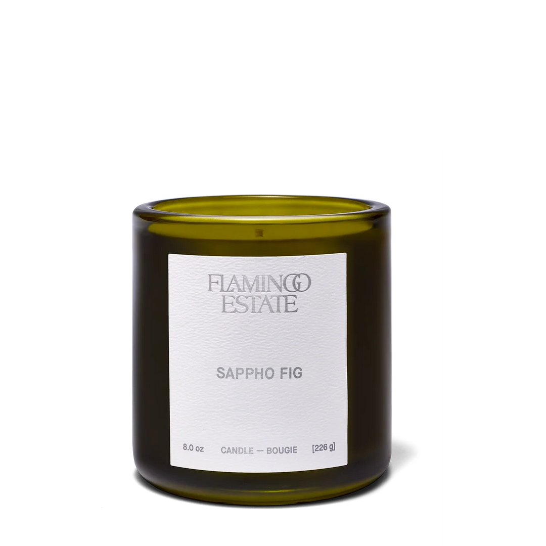 An 8.0 oz glass jar candle by Flaming Estate in the Sappho Fig scent, featuring an olive green glass container and a white paper label