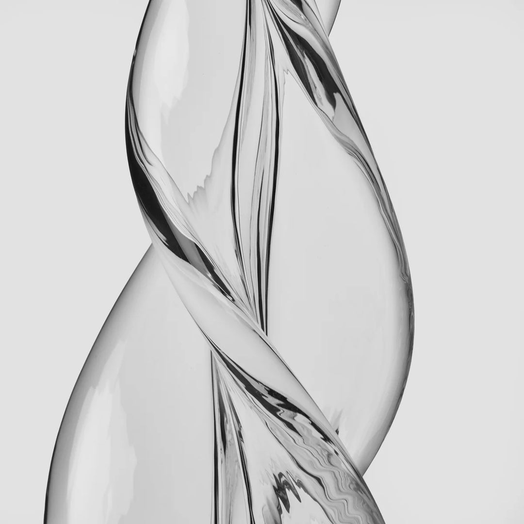 A close-up studio shot of a transparent sculptural glass object with a twisted, flowing form 