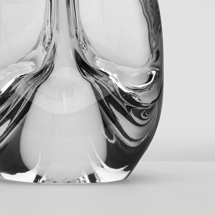 A close-up studio shot of a sculptural clear glass object with flowing, organic wavy forms and reflective highlights