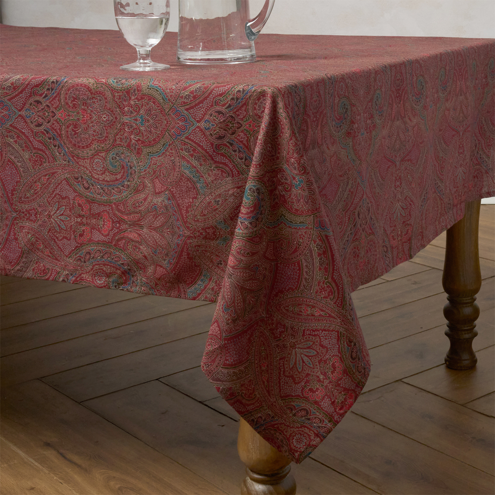 Red paisley patterned tablecloth on a wooden table with glasses and a pitcher.