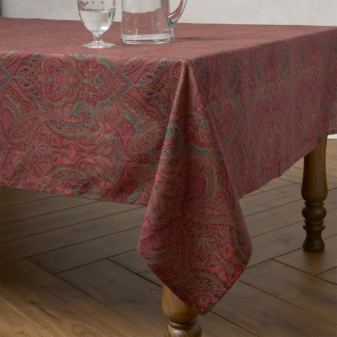 Red paisley patterned tablecloth on a wooden table with glasses and a pitcher.