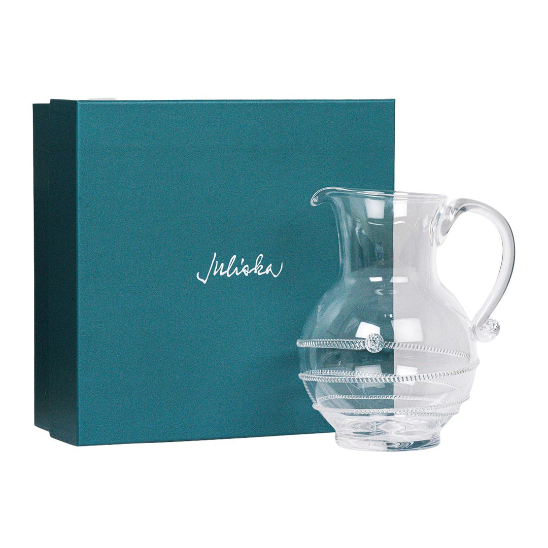 Clear glass pitcher with decorative rim next to a teal box with 'juliska' branding 