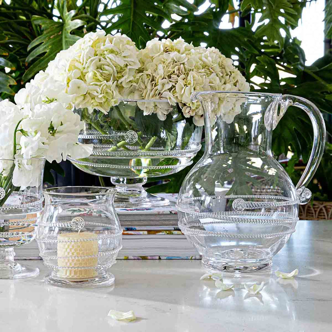 Clear glass pitcher and candle on a table with white flowers and books in the background