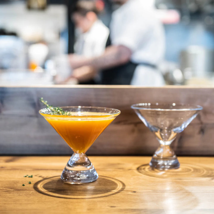Two cocktails in simon pearce martini glasses on a bar counter 