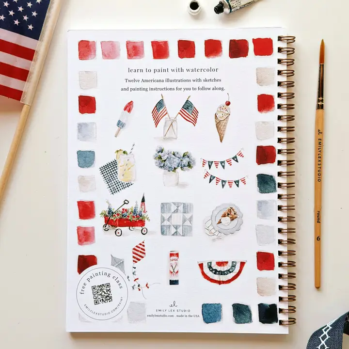 Notebook cover with watercolor illustrations and American flag, surrounded by art supplies.