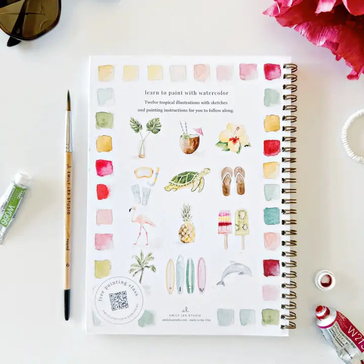 Artistic coloring book with watercolor illustrations on a white surface with art supplies.