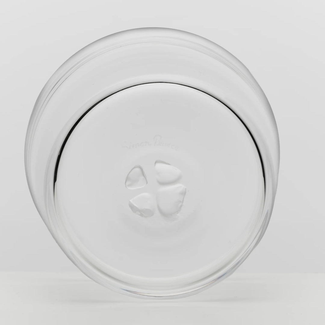 A clear glass plate viewed from above on a light gray background, showing a circular rim and a small embossed logo in the center.