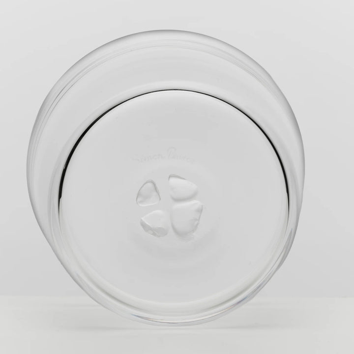 A clear glass plate viewed from above on a light gray background, showing a circular rim and a small embossed logo in the center.
