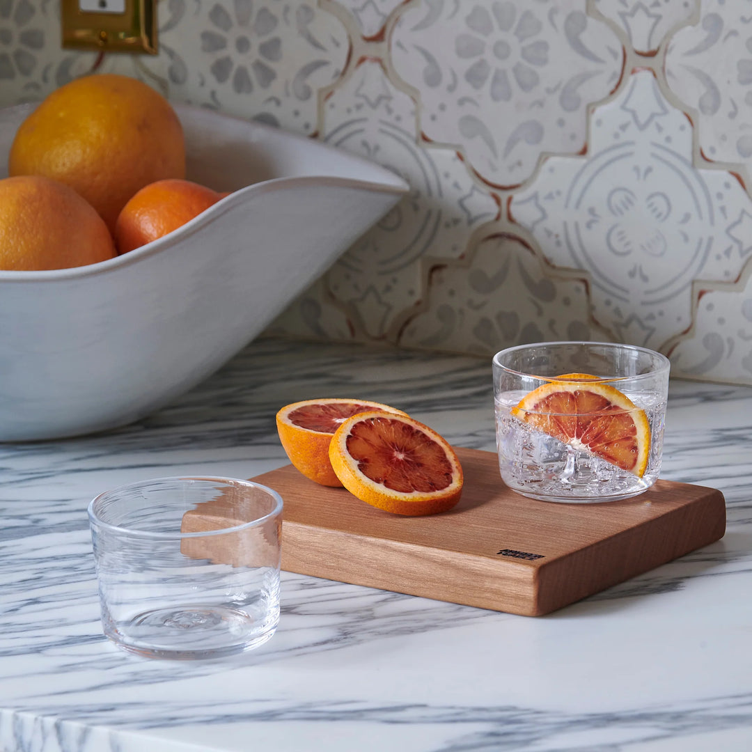 Bowl of oranges with a glass of water and sliced oranges on a cutting board.