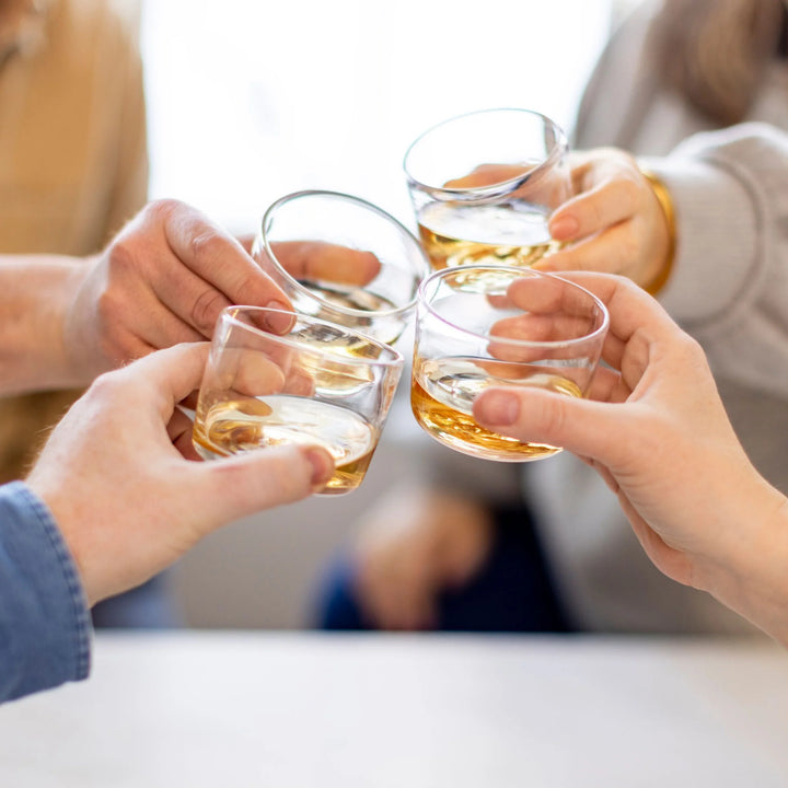 Four hands holding glasses of whiskey in a toast.