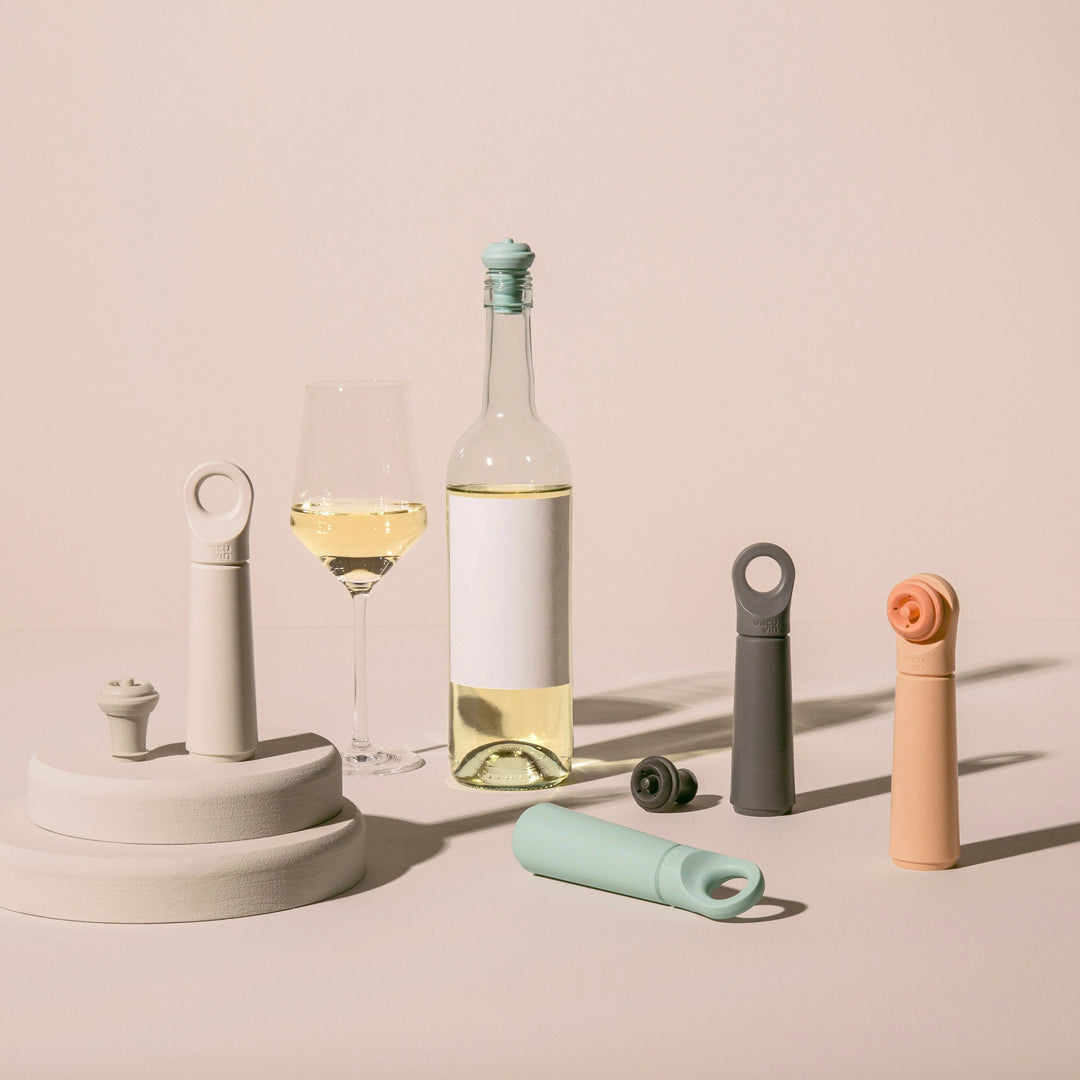 Wine bottle vacuum sealers in different colors next to a white wine bottle and glass