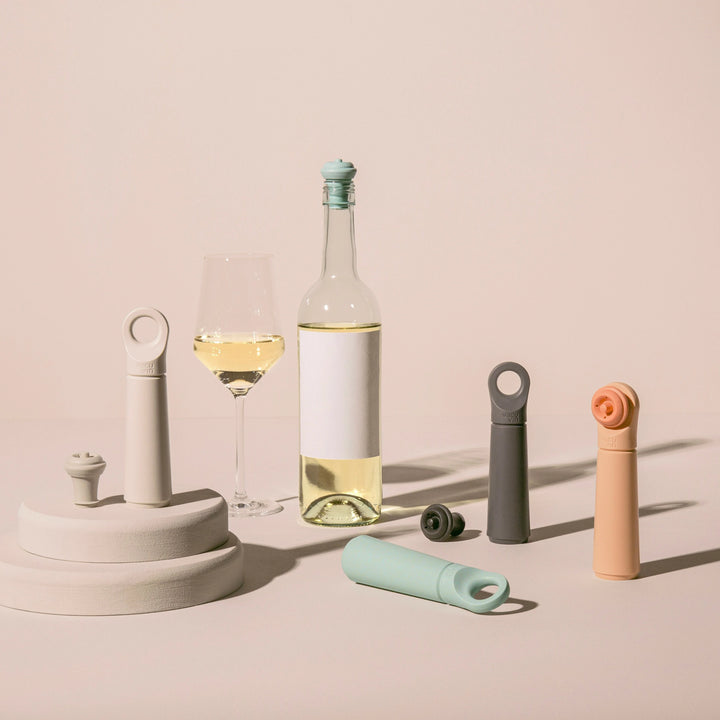 Wine bottle vacuum sealers in different colors next to a white wine bottle and glass