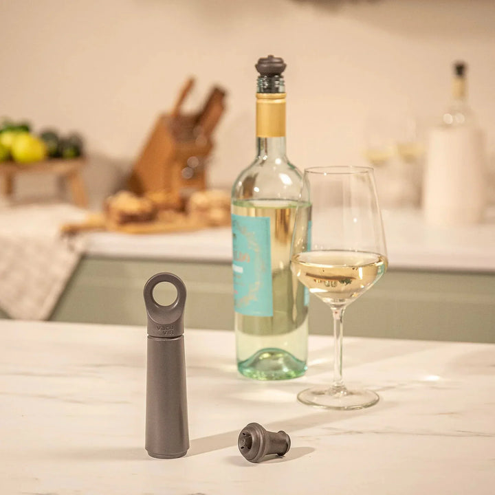 A white wine bottle and glass sitting behind a grey vacuum bottle sealer