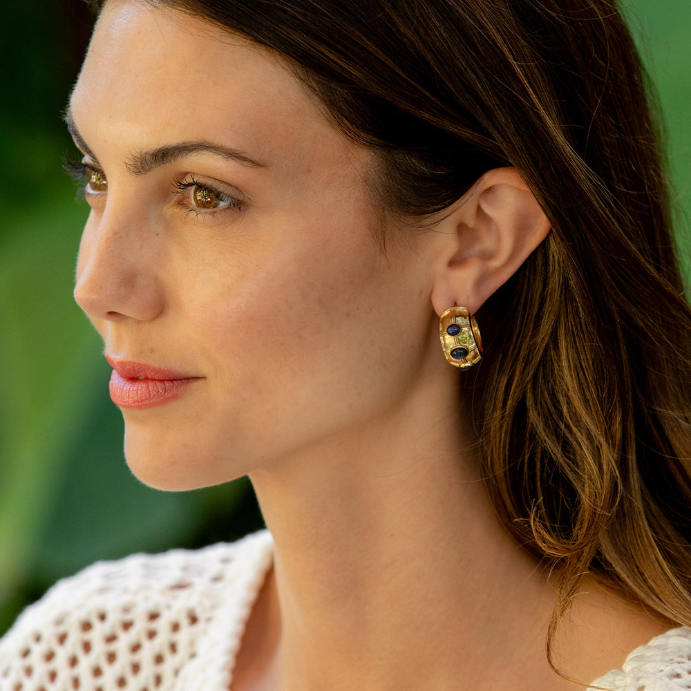 Close-up of a woman wearing gold earrings with green stones against a blurred green background