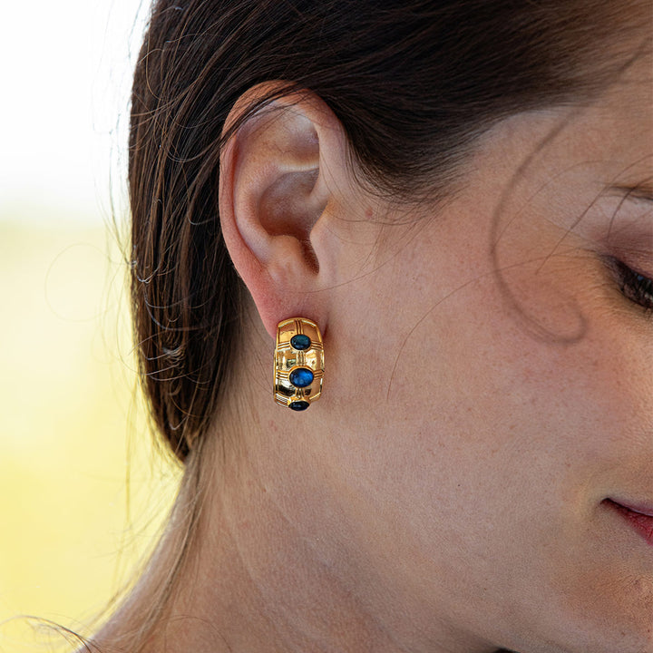 Close-up of a person wearing gold hoop earrings with blue stones.