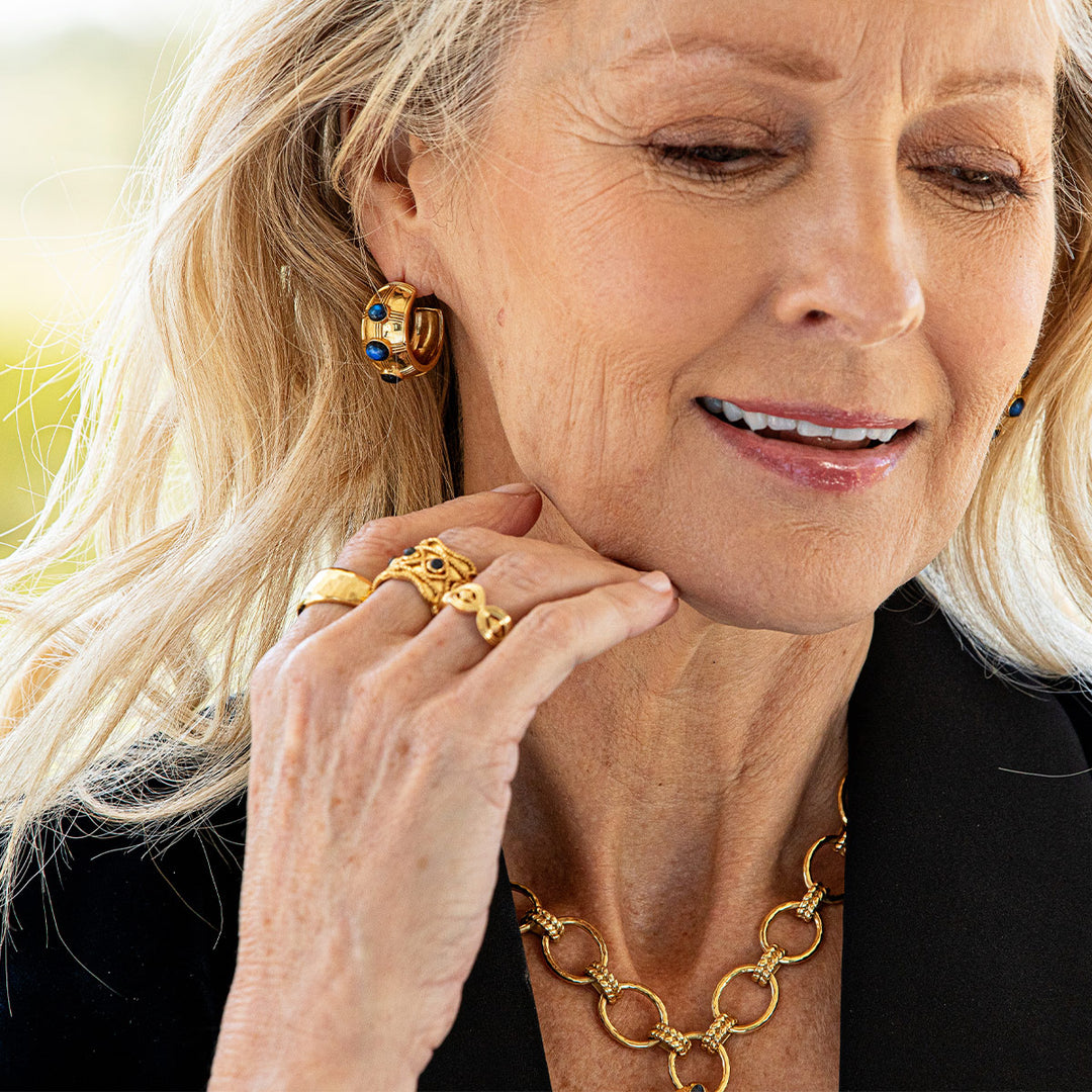 Woman wearing gold jewelry with blue stones including earrings, rings, and a necklace.