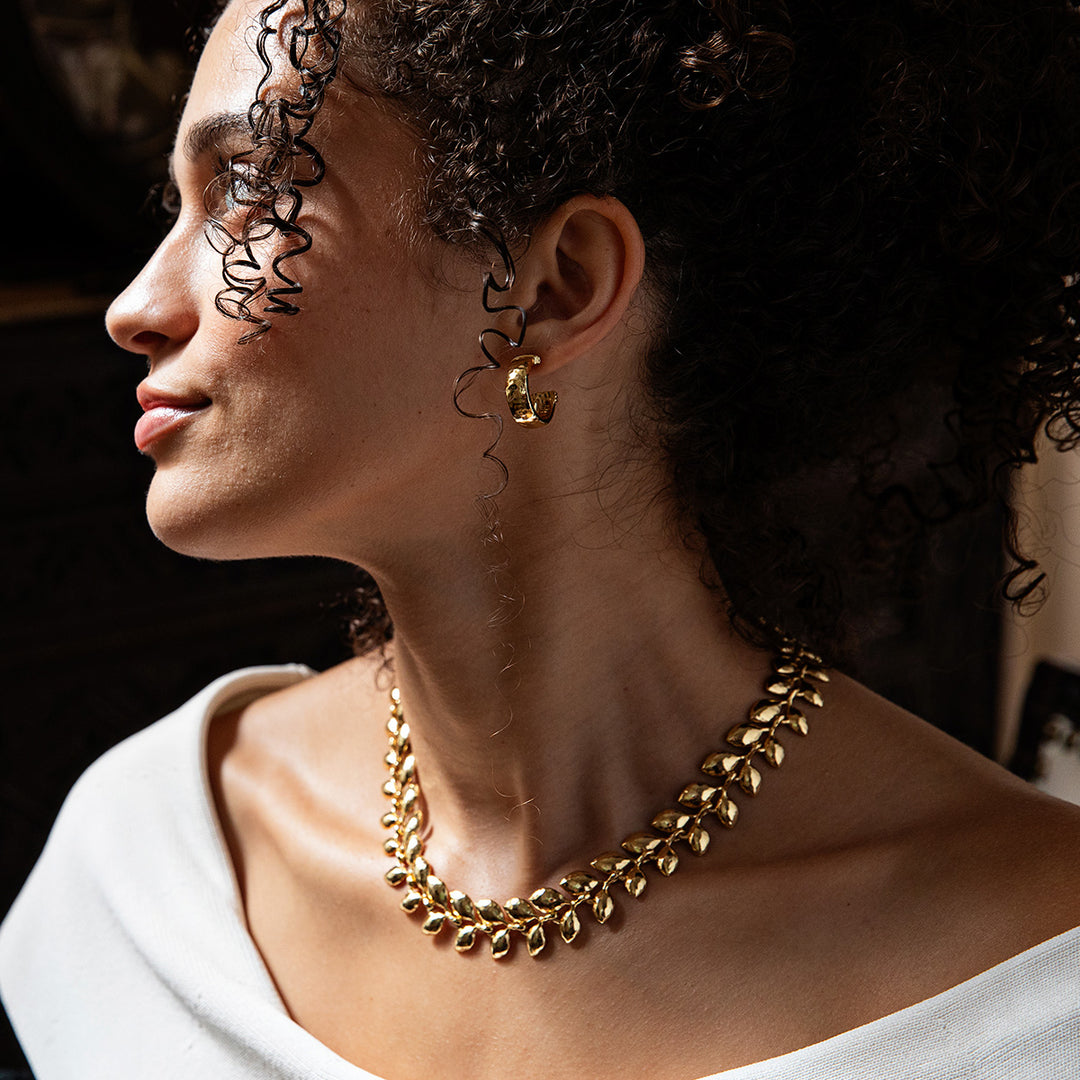 Woman wearing a gold necklace and earrings with a blurred background