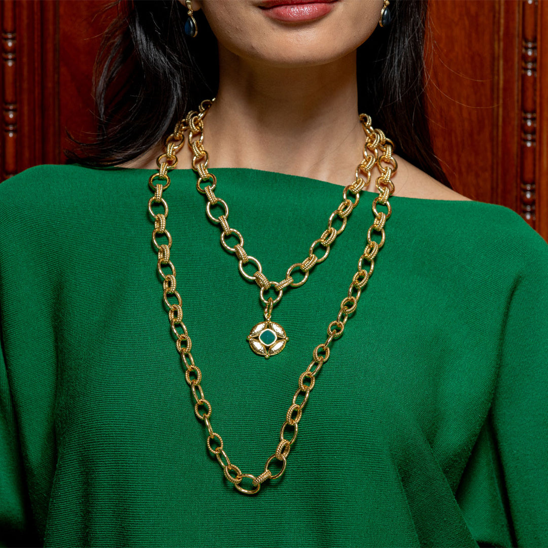 Gold chain necklace with a green gemstone pendant on a person wearing a green top.