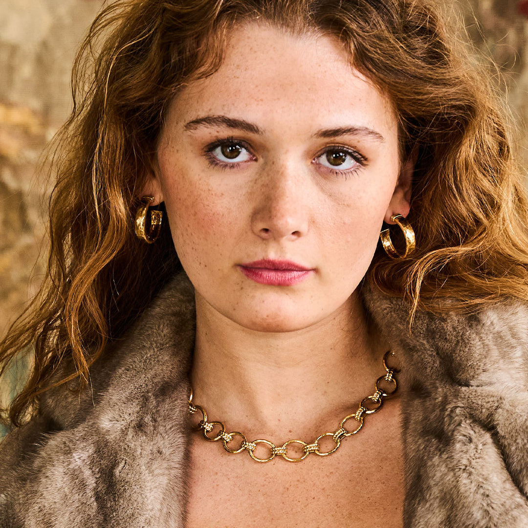 Woman wearing gold earrings and a gold chain necklace with a fur coat.