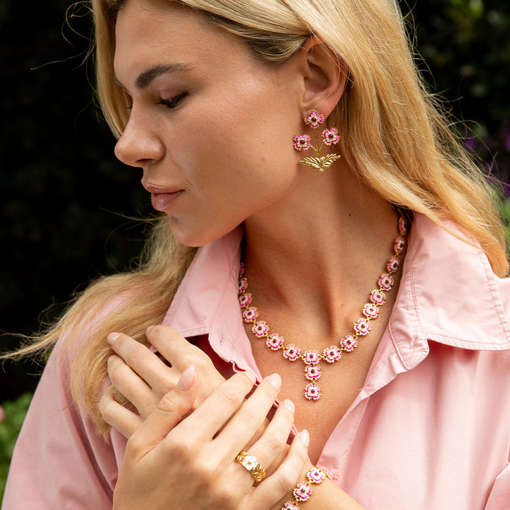 Woman wearing a pink floral necklace, earrings, and ring outdoors.