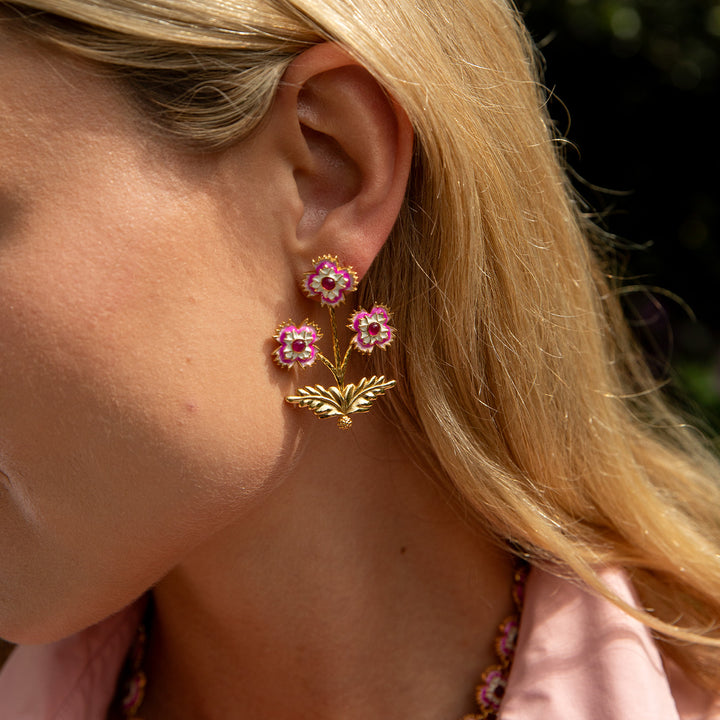 Close-up of a person wearing convertible gold floral earrings with pink gemstones.