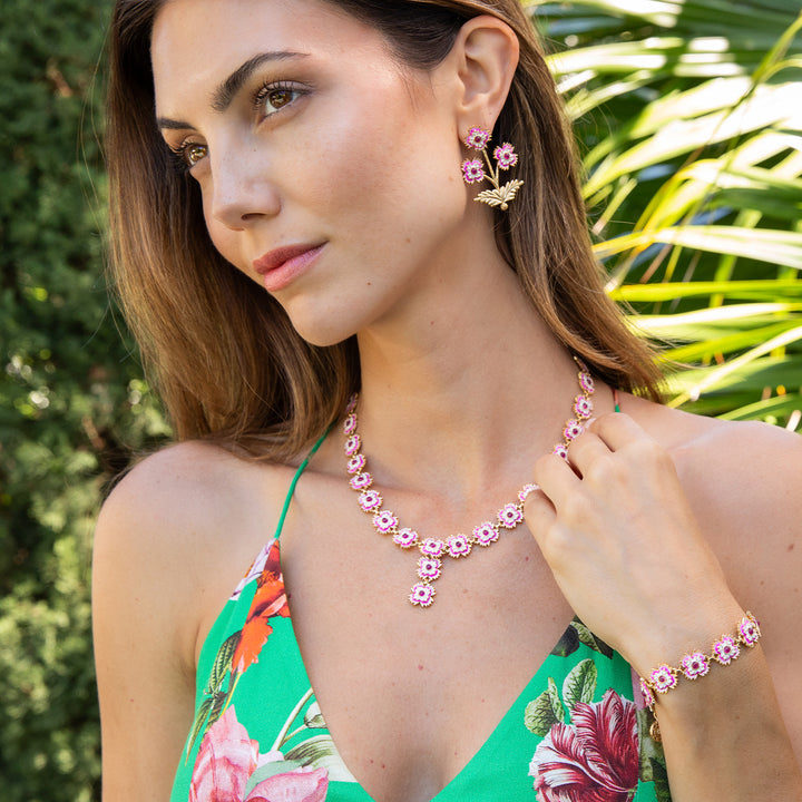 Woman wearing pink floral jewelry set against a green outdoor background