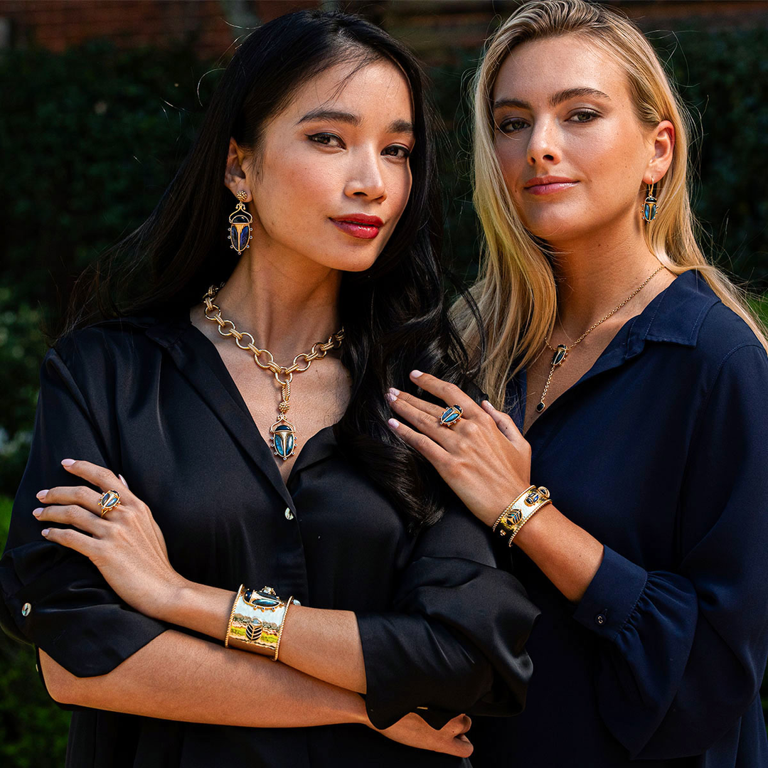 Two women posing together, wearing jewelry, with a blurred background