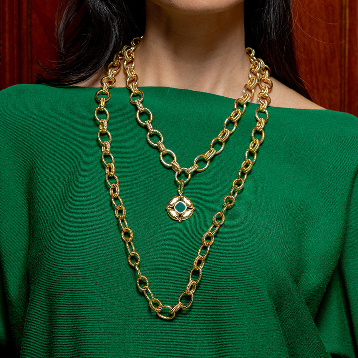 Gold chain necklace with a green pendant on a person wearing a green top.