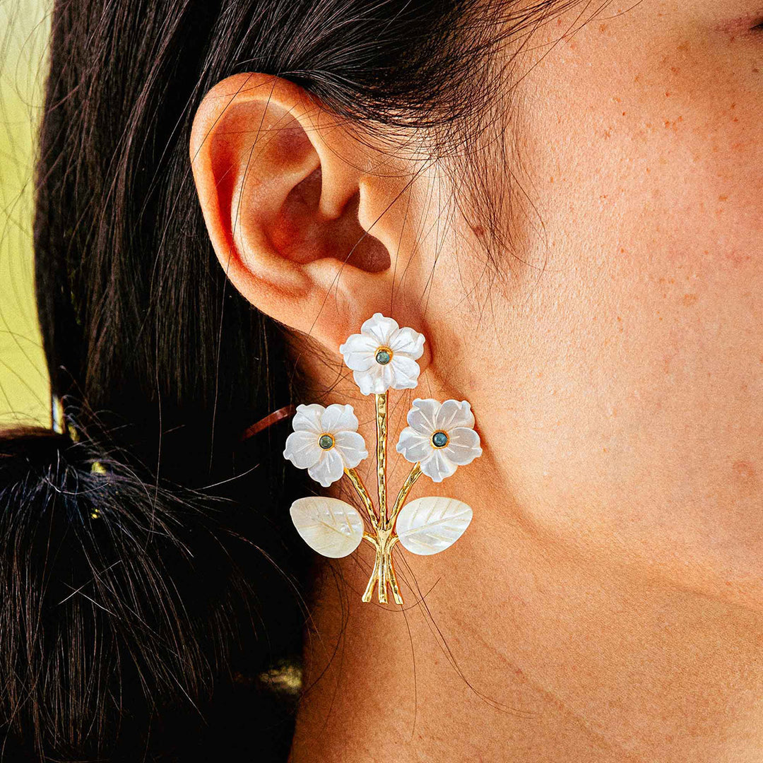 White floral earrings worn by a person with a blurred background