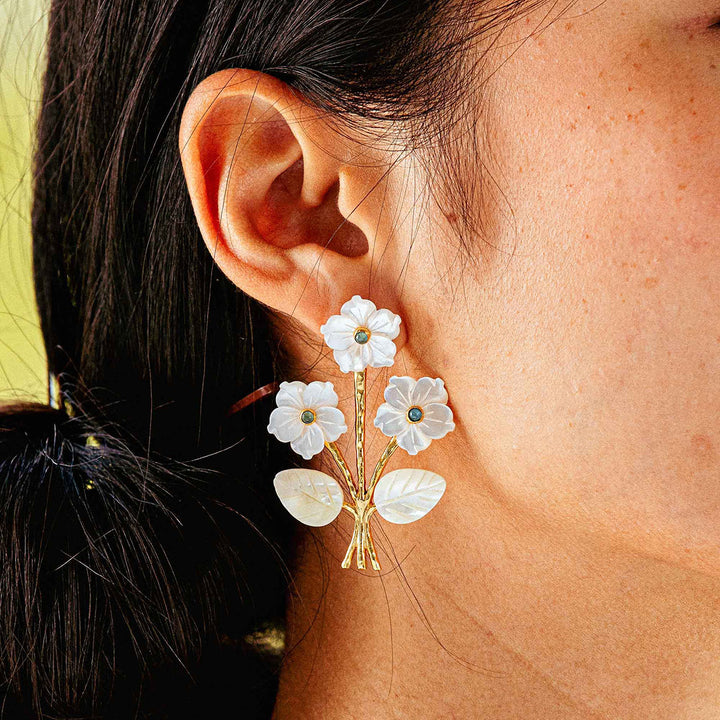 White floral earrings worn by a person with a blurred background