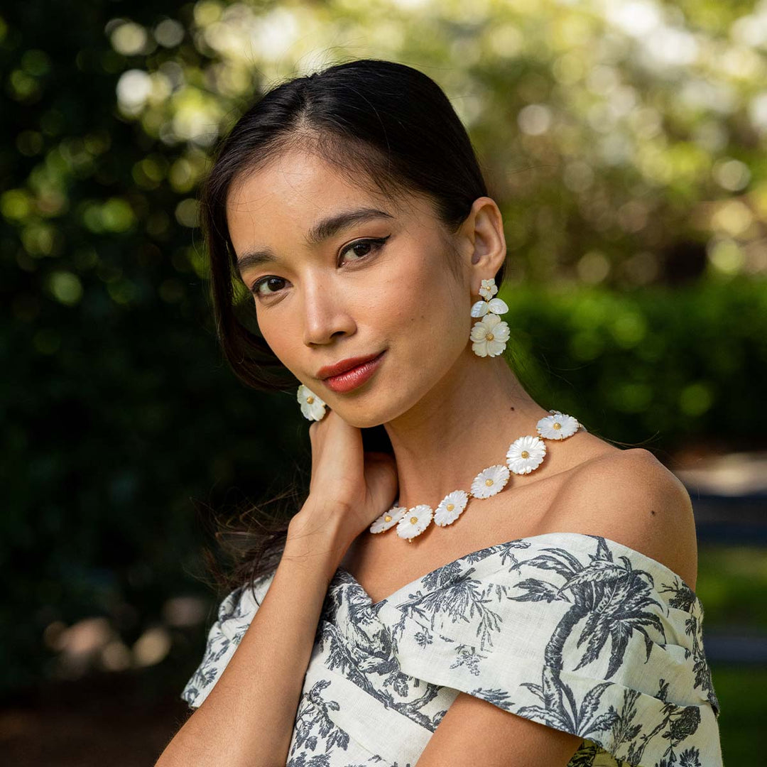 Woman wearing a floral off-shoulder top and matching jewelry daisy earrings and a necklace outdoors.