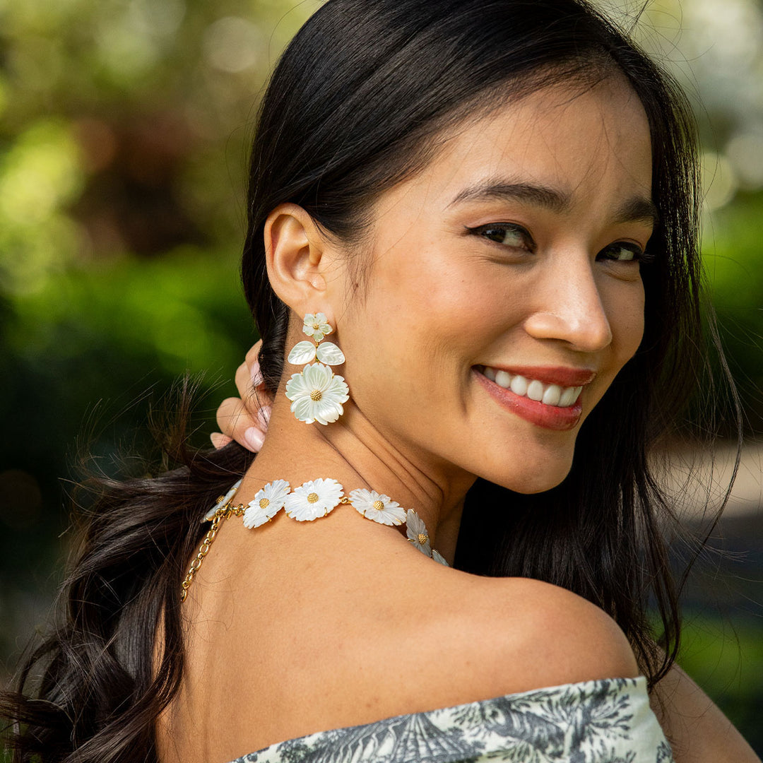 Woman wearing floral earrings and a necklace with a blurred green background