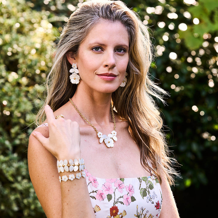 Woman wearing floral jewelry set outdoors with greenery in the background