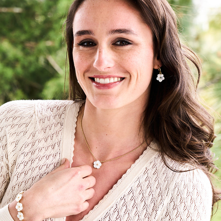 Woman wearing a white flower necklace with a matching earring and bracelet outdoors