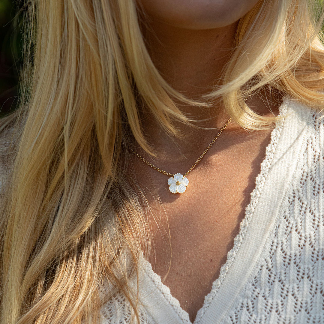 Close-up of a necklace with a white flower pendant worn by a person with blonde hair.