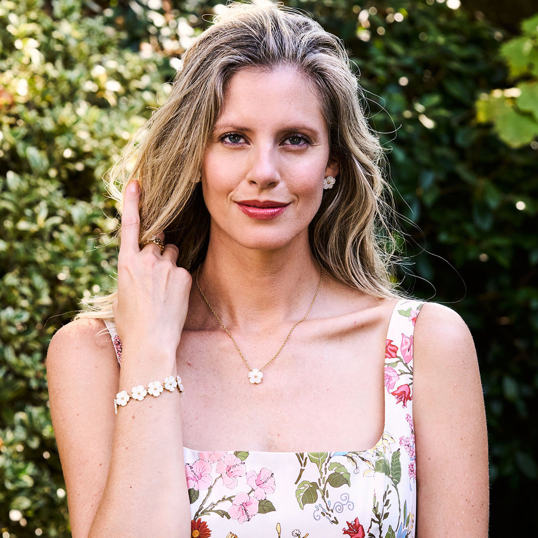 Woman wearing a floral dress and white floral jewelry with a green leafy background