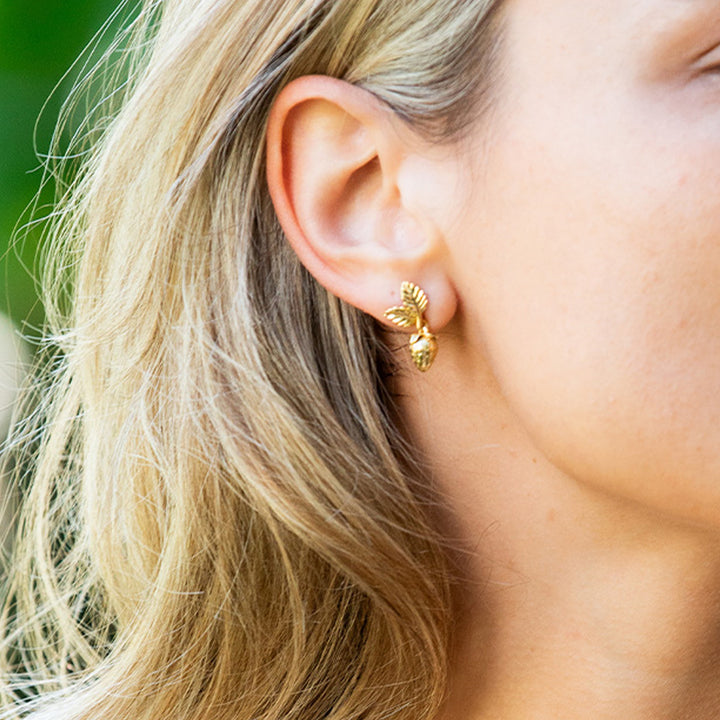 Close-up of a person wearing a gold strawberry earring with a blurred background