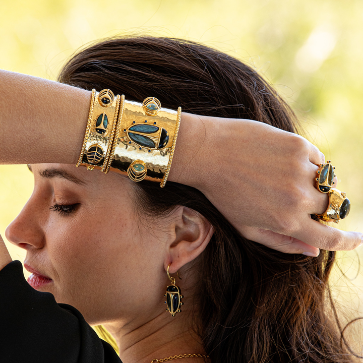Woman wearing gold jewelry with intricate designs against a blurred natural background