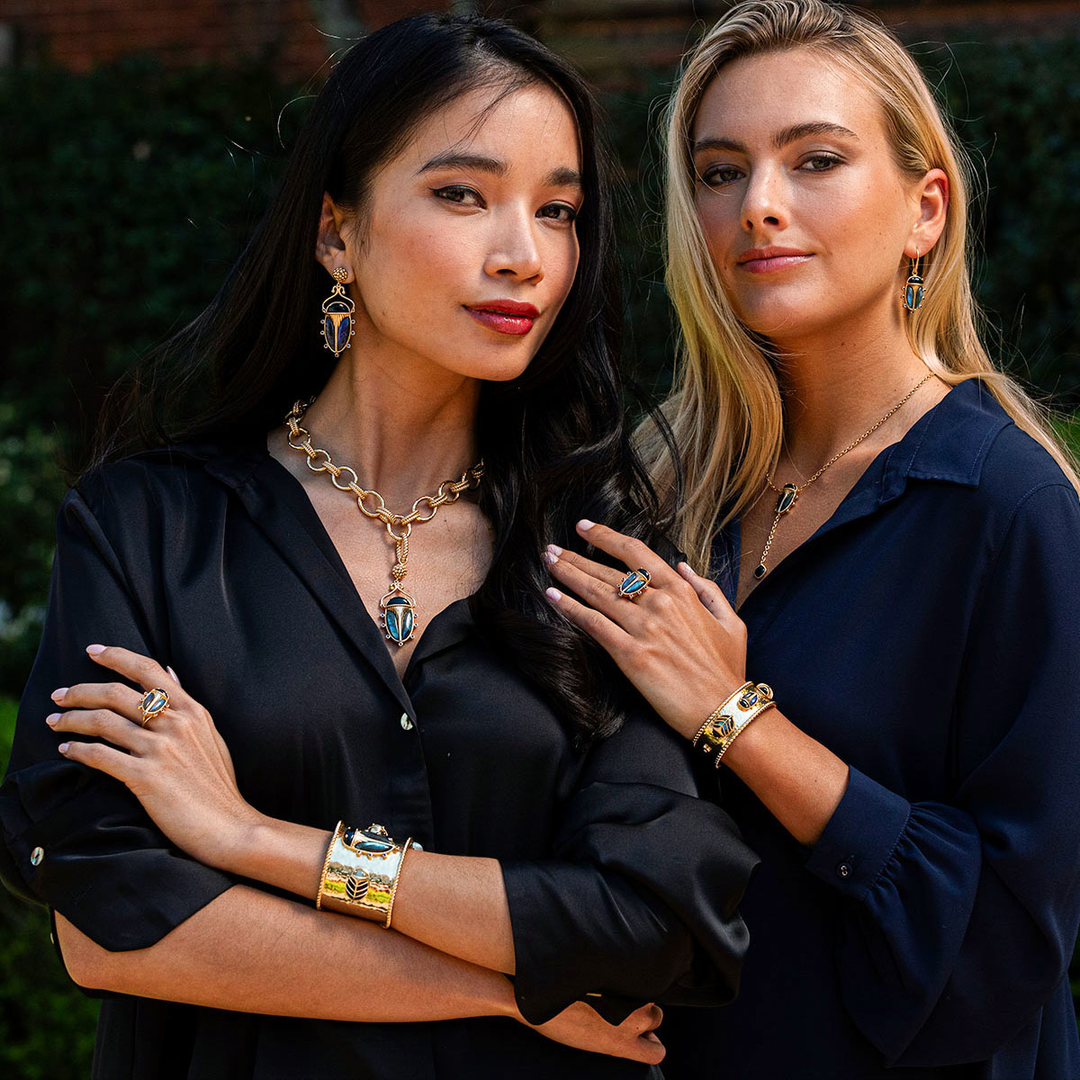 Two women posing together, wearing jewelry, with a blurred background